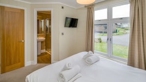 A hotel room with a bed, a TV, a shower, and a view of the outside.