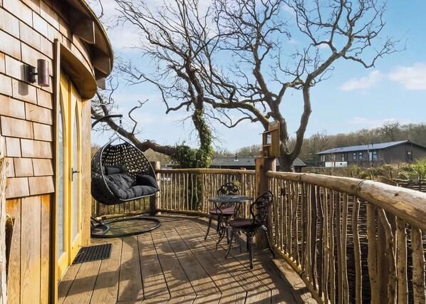 A wooden deck with a hanging chair, a table, and chairs.
