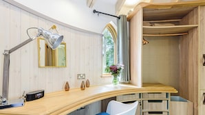 A modern bathroom with a wooden vanity, a mirror, a clock, and a window with a view of greenery.