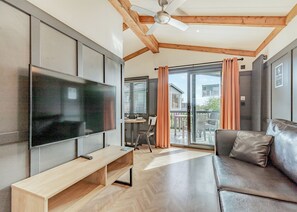 A modern living room with a flat-screen TV, wooden flooring, a leather sofa, and a balcony with a view of a house. - Dovedale Premier Lodge (Ashbourne)