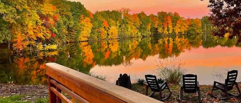 A wooden deck with a railing, overlooking a calm lake with autumn foliage.