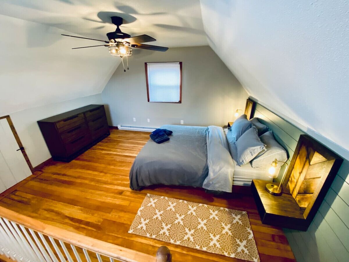 Ein Schlafzimmer mit Bett, Deckenventilator, Fenster und Nachttisch mit Lampe.