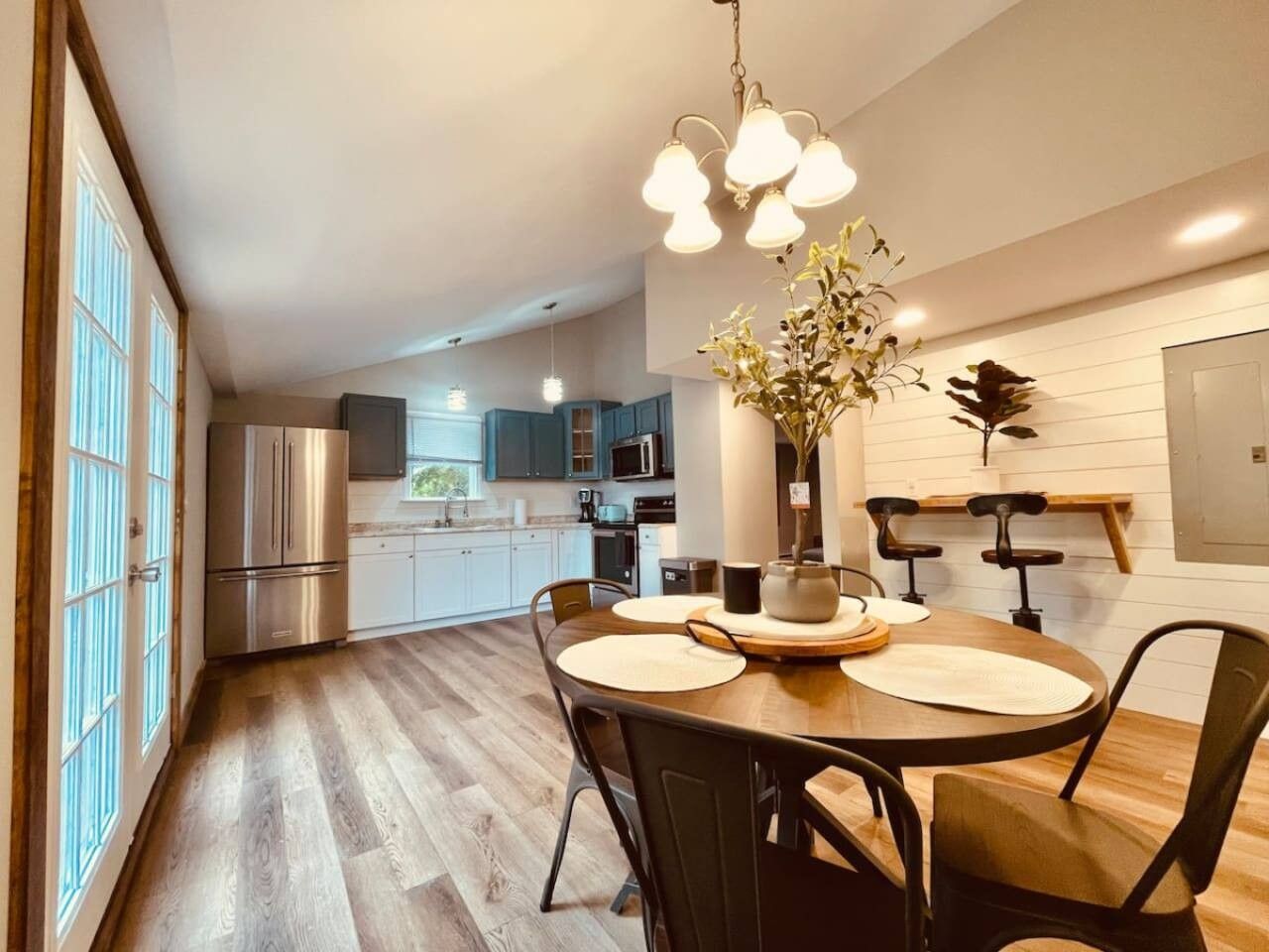 A modern kitchen with stainless steel appliances, a dining area with a wooden table and chairs, and a hanging light fixture.