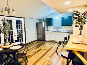 A modern kitchen with wooden flooring, a stainless steel refrigerator, and a dining area with a table and chairs. - #24 *Serenity* A Lakefront Cottage Retreat (Middletown)