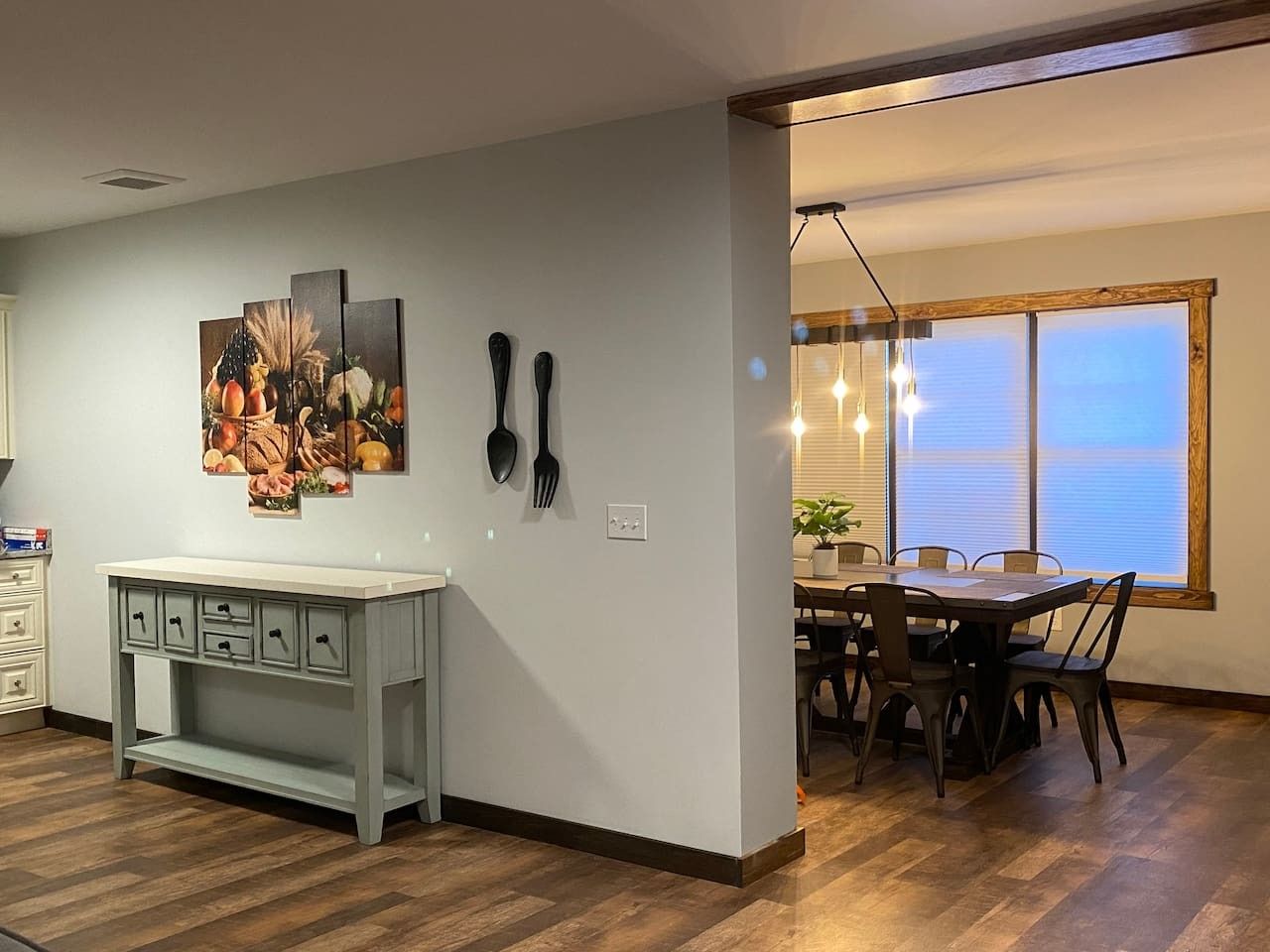 A dining area with a table and chairs, a painting on the wall, and a kitchen counter with drawers.