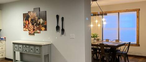 A dining area with a table and chairs, a painting on the wall, and a kitchen counter with drawers.