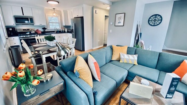 A modern living room with a blue sofa, a coffee table, and a dining area with a kitchen in the background.