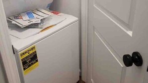 A compact laundry room with a washing machine and dryer, a door with a black handle, and a wooden floor.