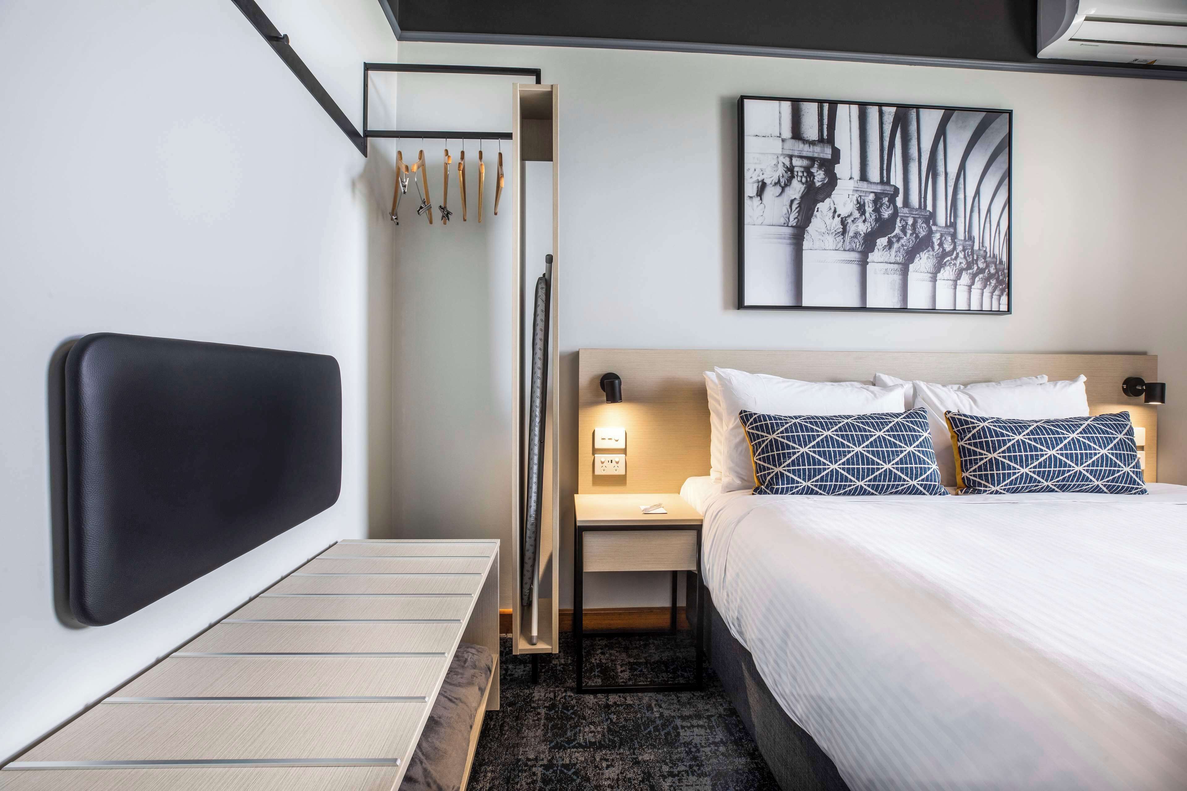 Una habitación de hotel moderna con cama, mesita de noche y perchero en la pared.