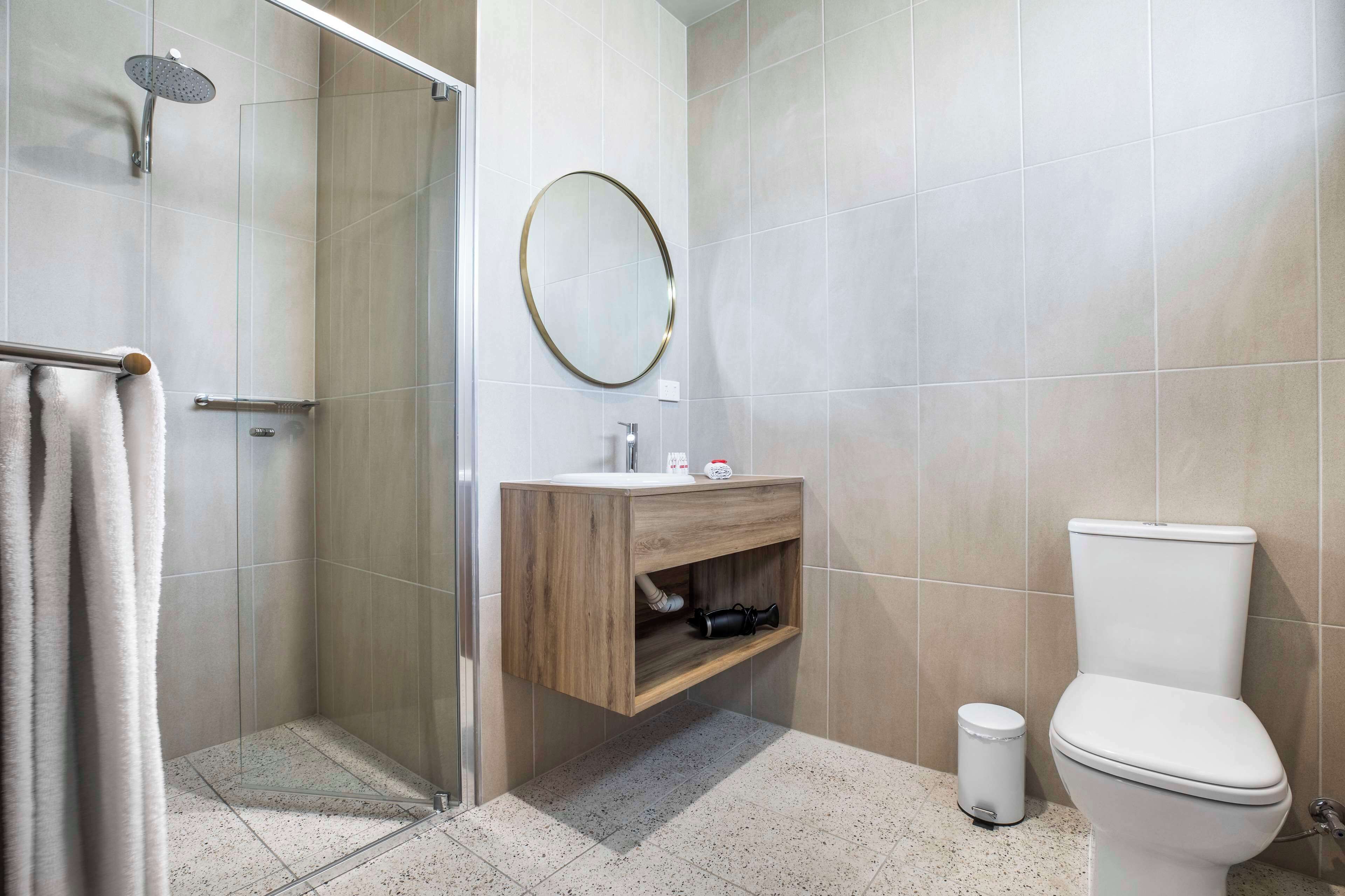 A modern bathroom with a glass shower enclosure, a wooden vanity, and a toilet.