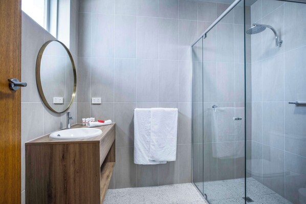 A modern bathroom with a wooden vanity, a round mirror, a white sink, and a glass-enclosed shower area.