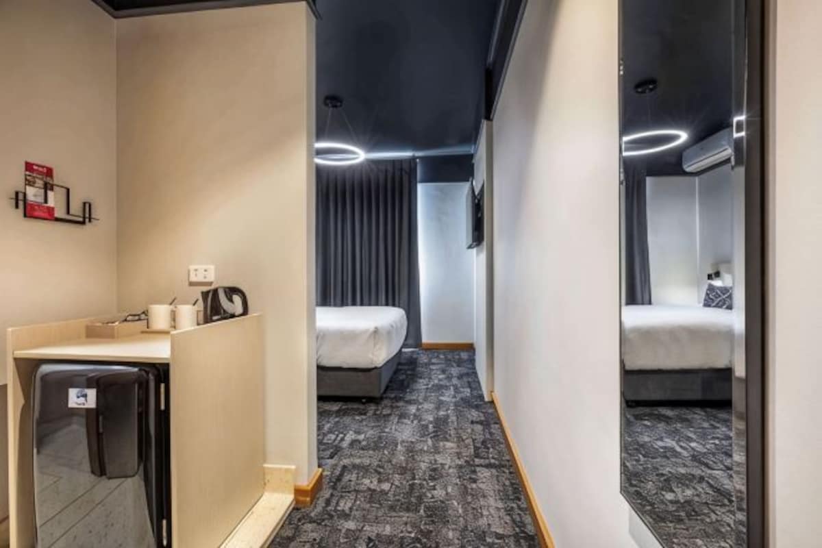 A hotel room with a desk, a bed, a small seating area, and a bathroom.