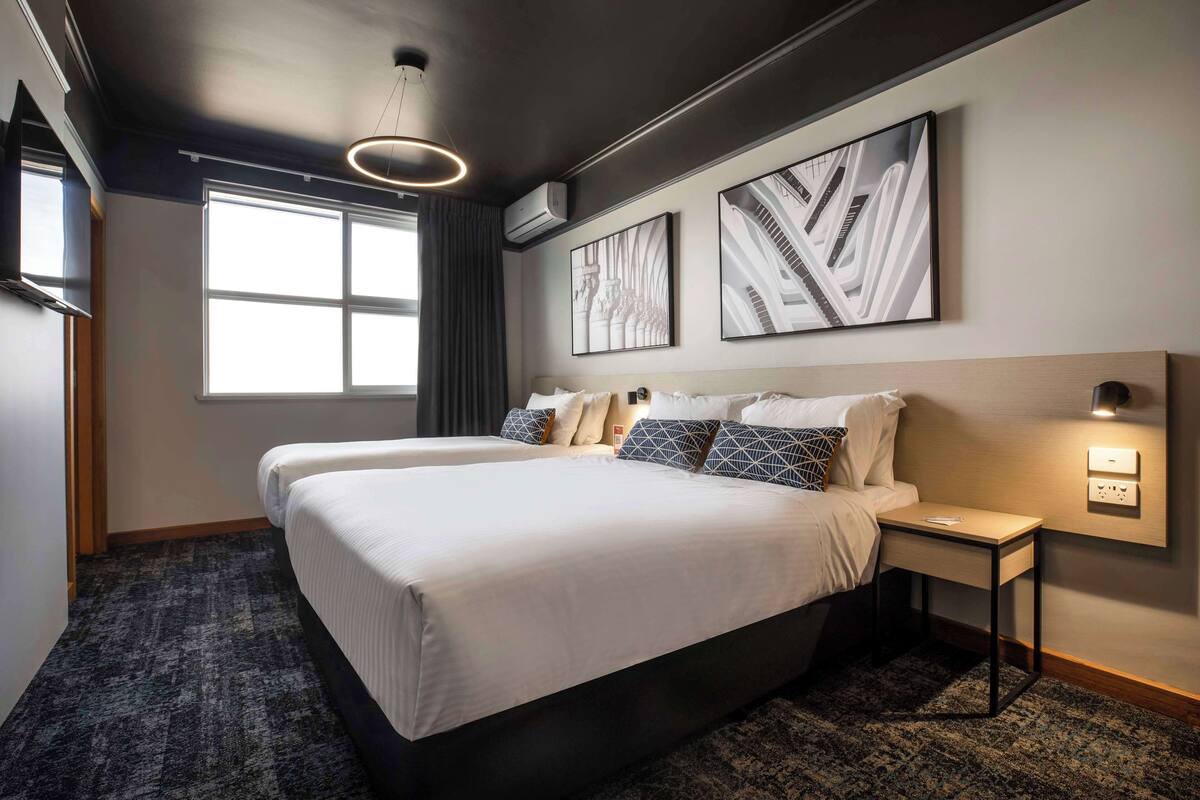 Habitación de hotel con una cama grande, dos mesitas de noche, aire acondicionado en la pared y una ventana con cortinas.