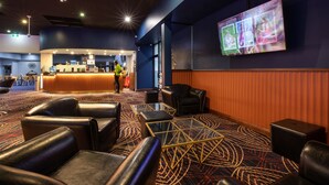 A hotel lobby with leather seating, a reception desk, a large screen displaying sports content, and a patterned carpet. - Nightcap at Empire Hotel (Kilburn)