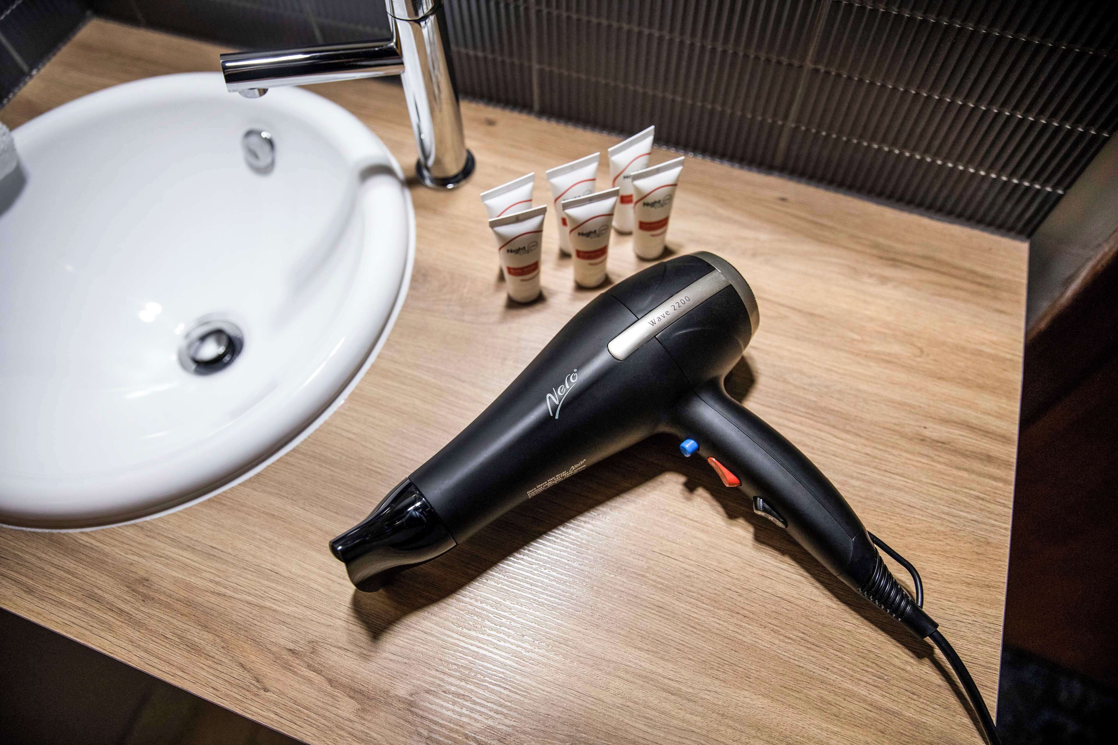 A hair dryer and several tubes on a wooden countertop near a sink.
