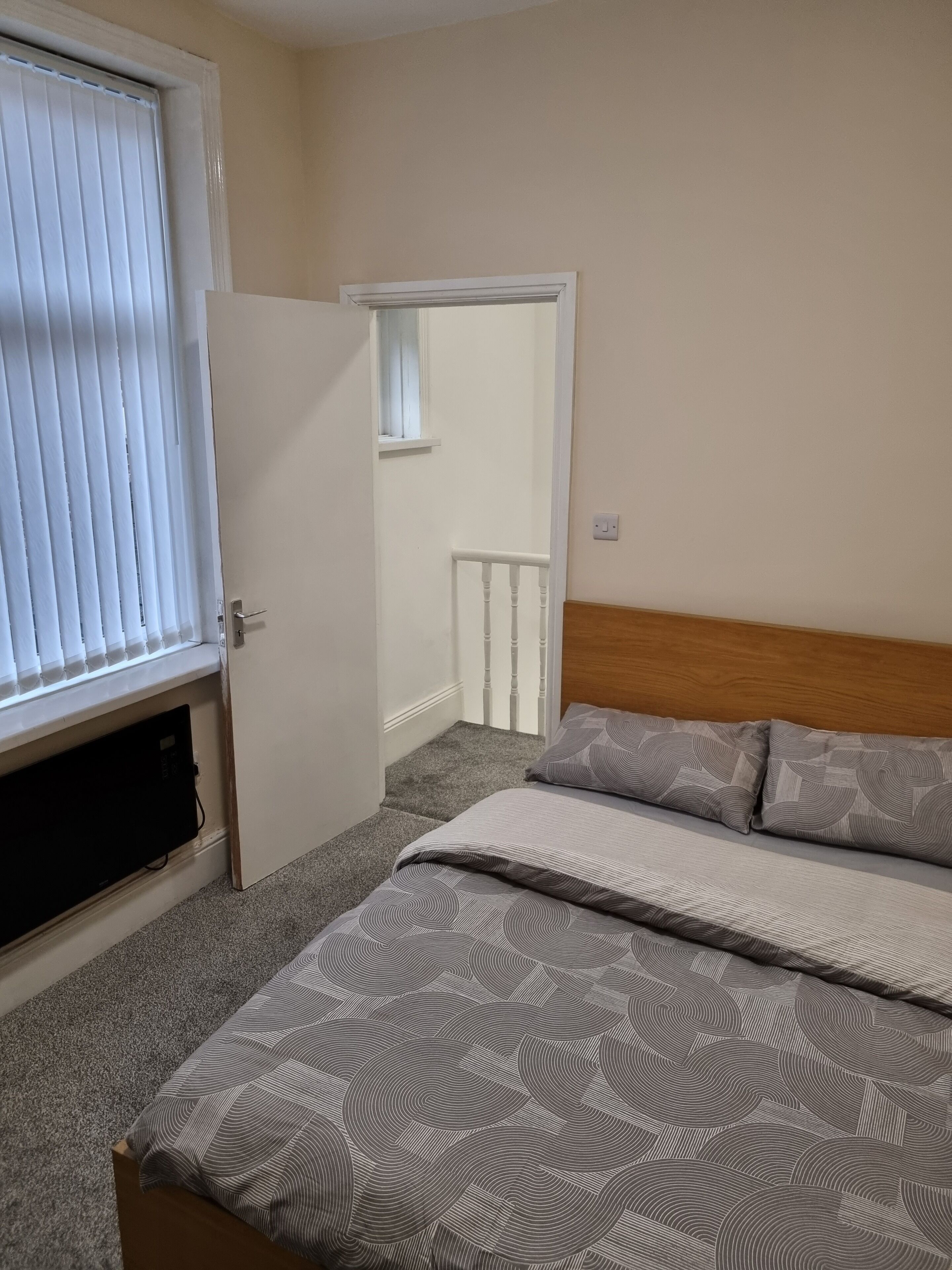 A bedroom with a bed, a window with blinds, a door, and a small window above the door.