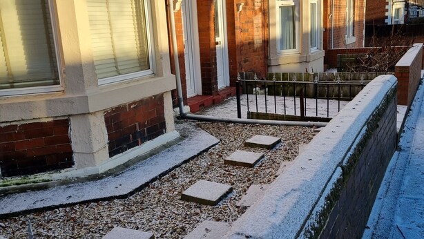Een woonwijk met bakstenen huizen, een met sneeuw bedekte looppad en een metalen hek.
