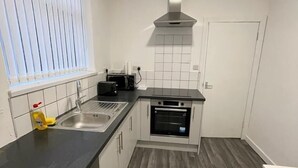 Een compacte keuken met een zwart aanrechtblad, witte kastjes, een roestvrijstalen spoelbak en een inbouwoven.