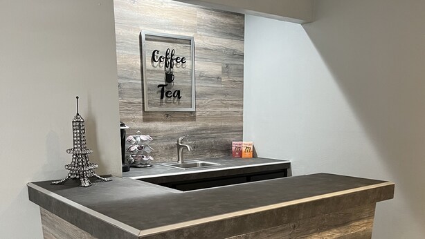 A modern kitchen with a bar area, featuring a wooden backsplash, a coffee and tea sign, and a small Eiffel Tower decoration.