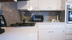 A kitchen with white cabinets, a gas stove, a built-in oven, and a backsplash of dark tiles.