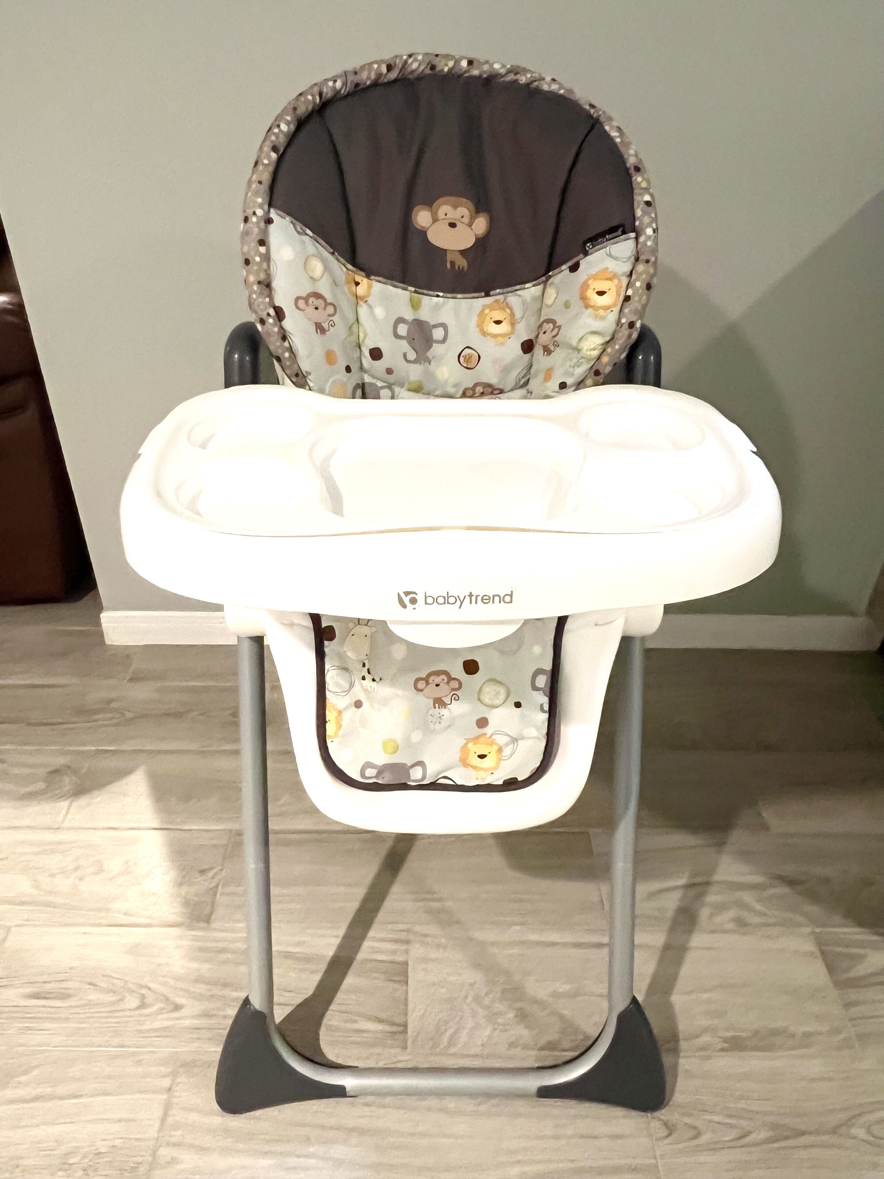 Een baby hoogstoel met een beklede zitting met patroon en een witte lade.