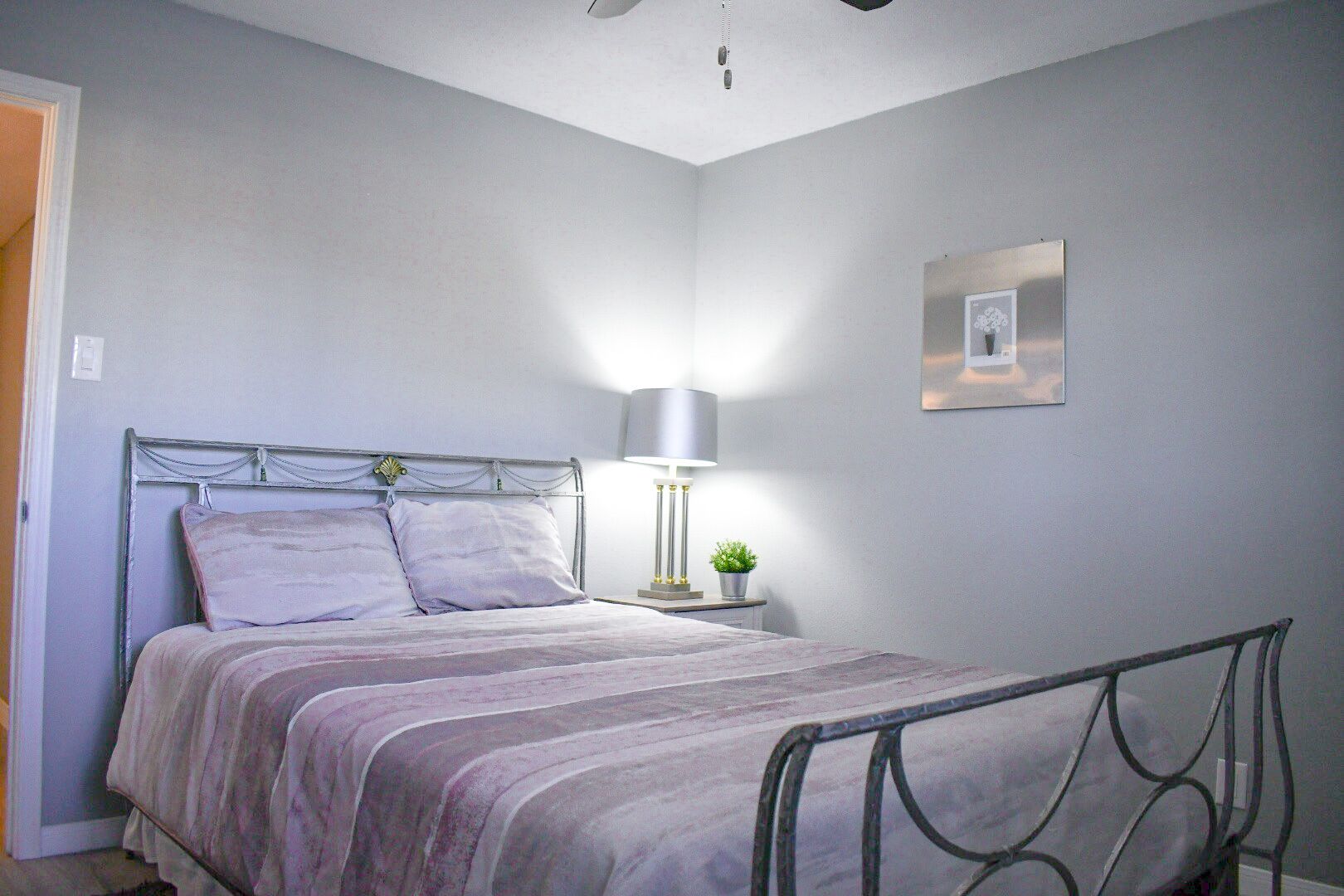 Ein Schlafzimmer mit einem Metallbettgestell, einem Nachttisch mit Lampe und einer kleinen Topfpflanze.