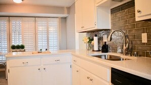 A kitchen with white cabinetry, a stainless steel sink, and a backsplash with dark tiles.