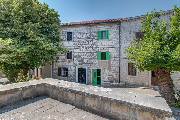 A stone building with a tiled roof, green shutters, and a central door. - Lovely 15th Century apartment in Osor (Osor)