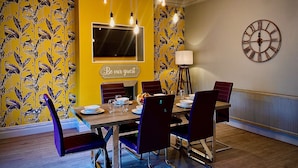 A dining area with a yellow wall, a clock, and a 'Be our guest' sign.