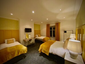 Ein Hotelzimmer mit zwei Betten, einem Schreibtisch, einem Stuhl, einem Fernseher und einem Fenster mit Vorhängen.