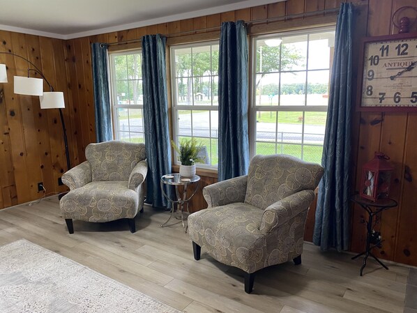 A room with two patterned armchairs, a small round table, a potted plant, and a wall clock.