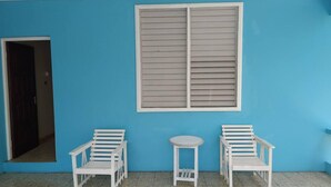 A room with a blue wall, a window with blinds, two white chairs, and a small round table.