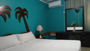 A bedroom with a bed, a nightstand, a dresser, a mirror, and a wall with palm tree decorations.