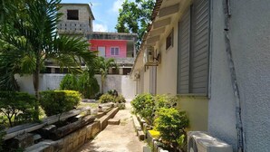 A narrow pathway flanked by buildings, with a small garden area on one side and a parked vehicle on the other.