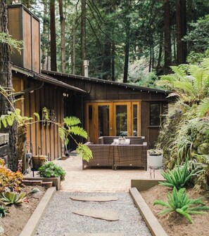 Una cabana de fusta moderna amb zona de terrassa, envoltada per un bosc dens.