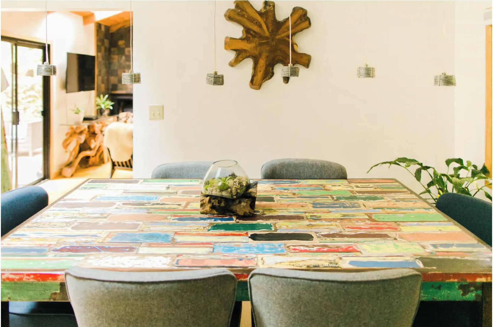 A dining table with a colorful, abstract tablecloth, surrounded by four grey chairs.