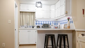 A kitchen with white cabinets, a blue and white backsplash, a toaster, and two black stools. - Lake Access / Private Boat Launch Cabin with Game Room! (Scottsboro)
