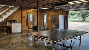 A spacious room with a ping pong table, a refrigerator, a microwave, and a staircase leading to another level. - Lake Access / Private Boat Launch Cabin with Game Room! (Scottsboro)