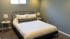 Un dormitorio con una cama, dos mesitas de noche con lámparas, un ventanal y suelo cubierto de alfombra.