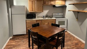 Cocina compacta con armarios de madera, microondas, estufa y una mesa de comedor con sillas.