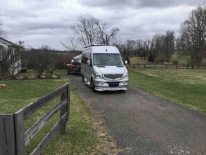 A silver van parked on a rural road with a wooden fence on the left.