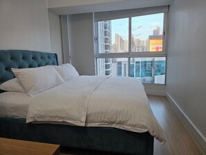 A bedroom with a bed, a window with a city view, and a blue headboard.