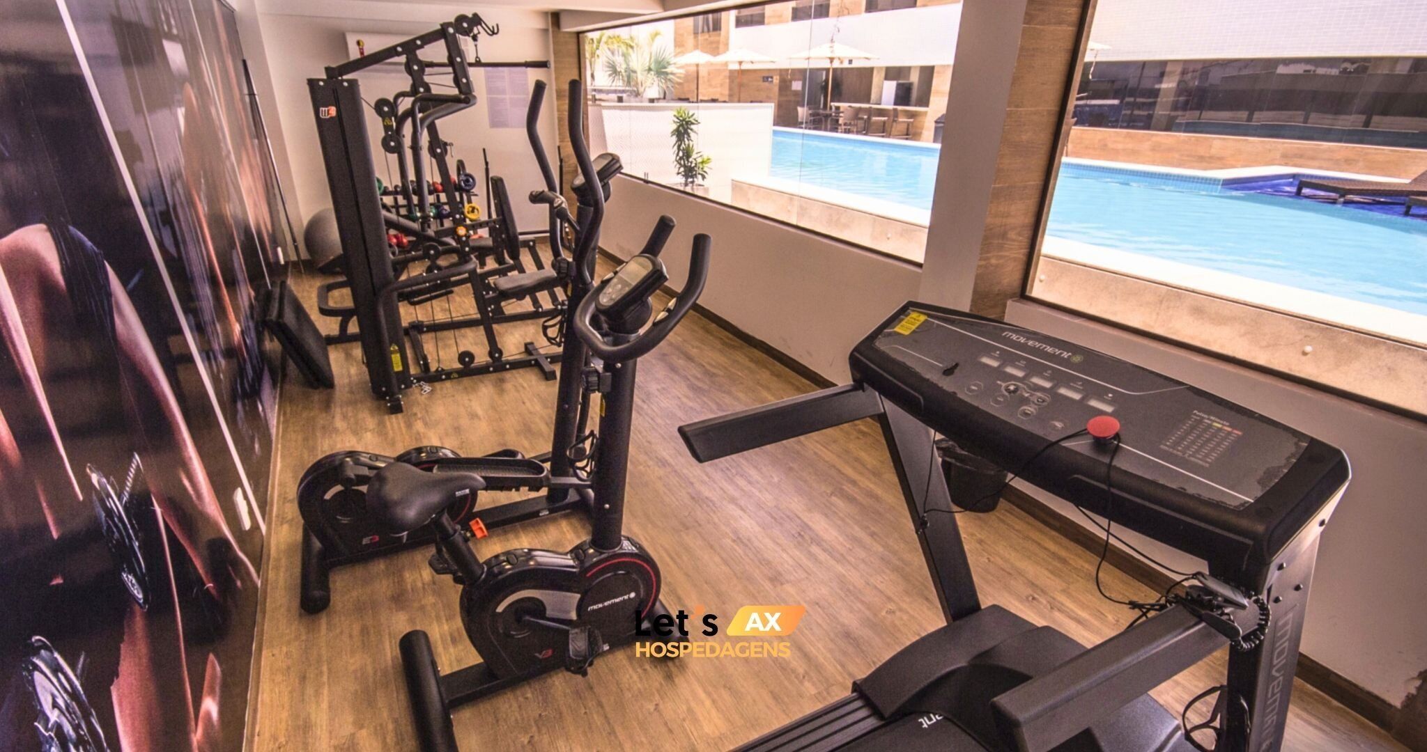 A gym with cardio machines, weight equipment, and a pool visible through the window.