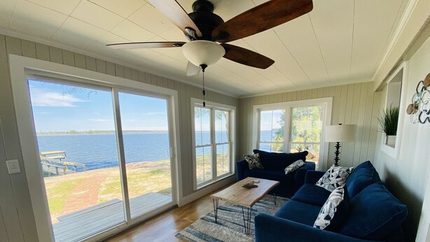 A spacious living room with a large sliding glass door leading to a deck overlooking a body of water. - Lake Marion Lakehouse with 180° lake view (Elloree)