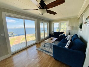 A spacious living room with a large sliding glass door leading to a deck overlooking a body of water.