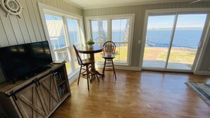 A spacious room with a large TV, wooden cabinets, a dining table with chairs, and large sliding glass doors leading to a view of the water. - Lake Marion Lakehouse with 180° lake view (Elloree)
