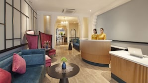 A modern hotel lobby with a reception desk, seating area, and a view into the dining area.