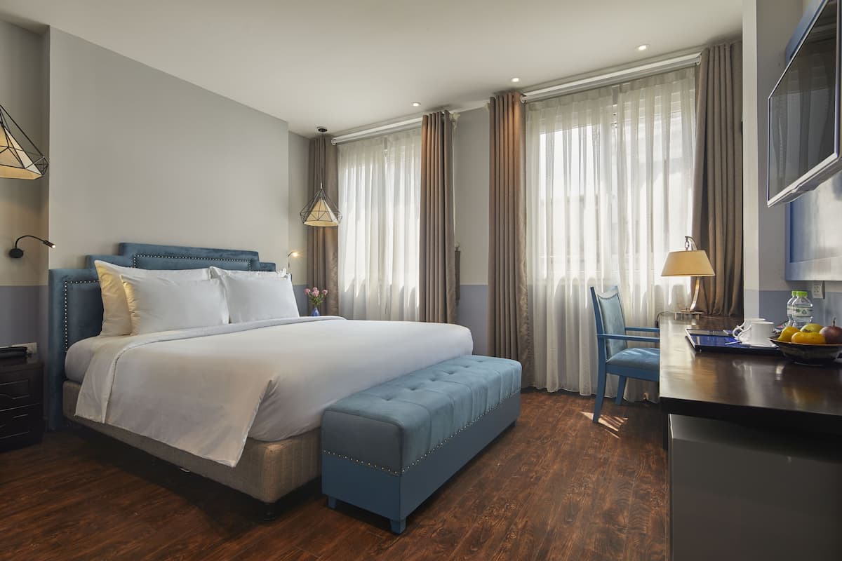 Una habitación de hotel moderna con una cama grande, un banco azul, un escritorio con lámpara y una televisión.