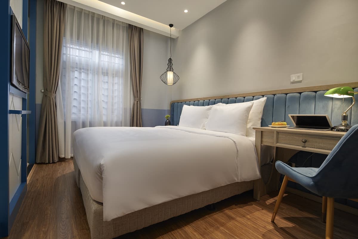 Una habitación de hotel moderna con una cama grande, un escritorio con una computadora portátil, una silla y una lámpara colgante.