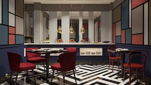 A modern dining area with a checkered floor, red upholstered chairs, and a central island with a display of food.